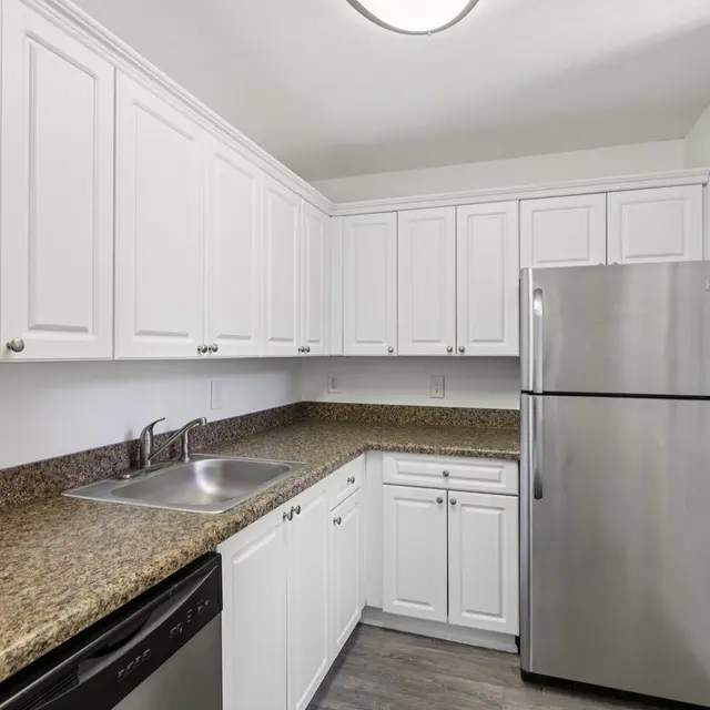 A modern kitchen featuring white cabinets, a stainless steel refrigerator, and a granite countertop.