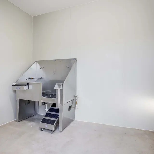 A modern pet grooming area with a stainless steel grooming station and stairs, situated in a clean and spacious room with white walls.