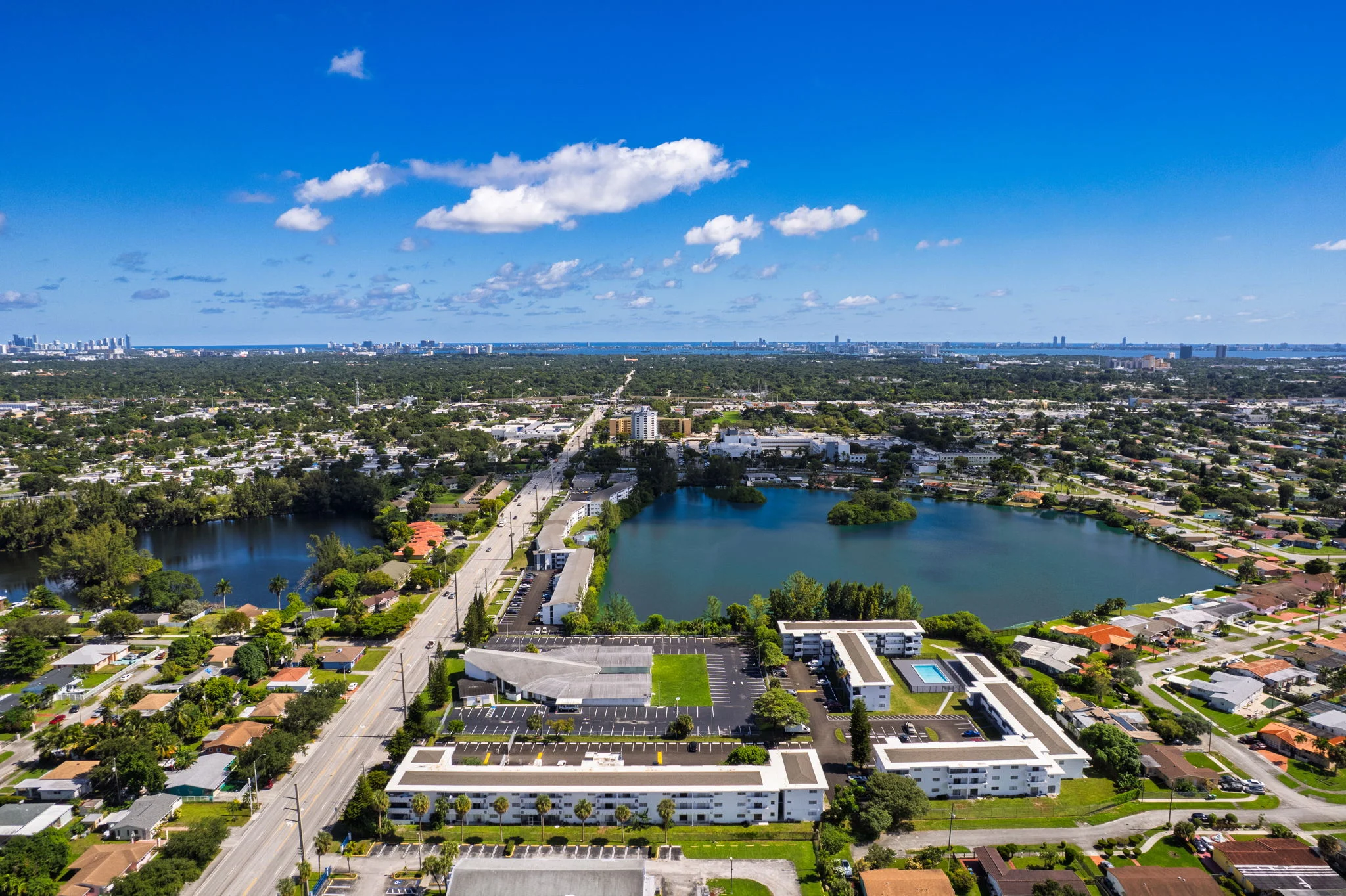 Aerial view of a suburban area featuring residential buildings, roads, and lakes under a clear blue sky.
