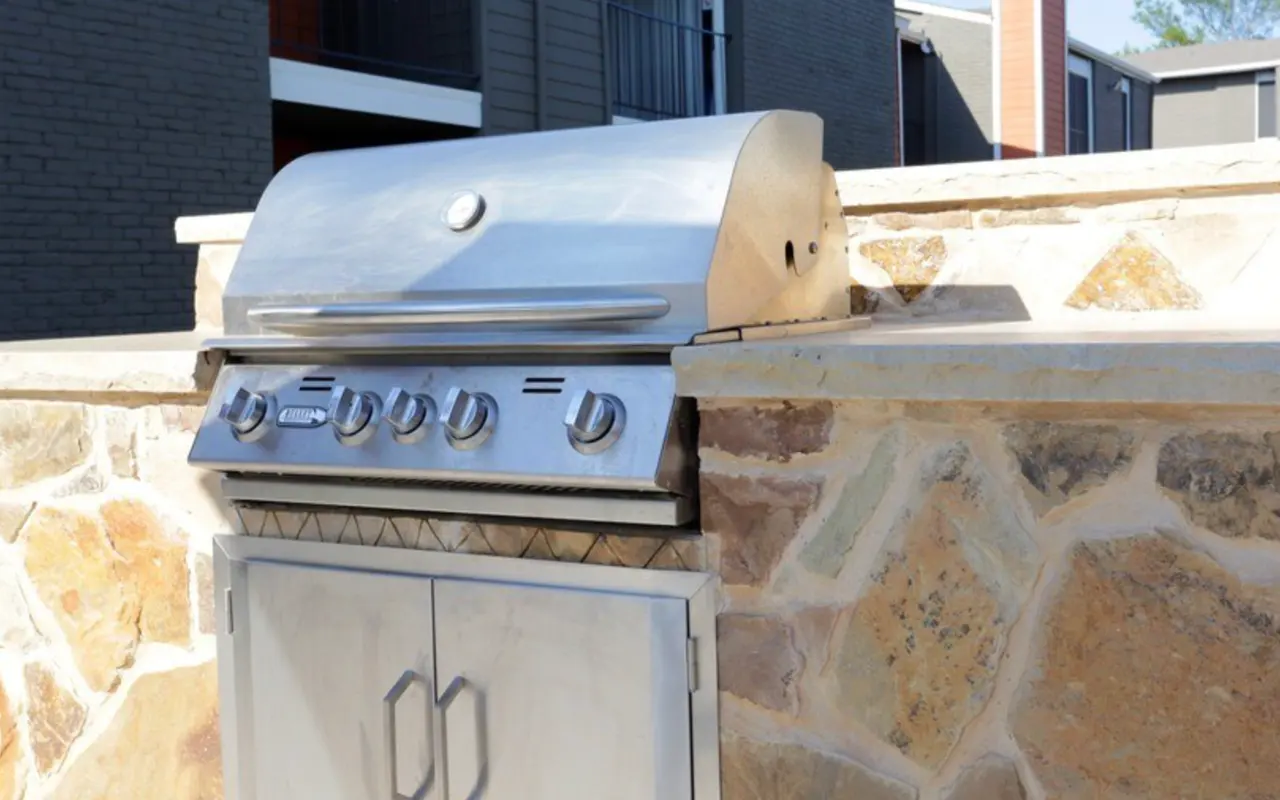 A stainless steel outdoor grill housed in a stone wall.