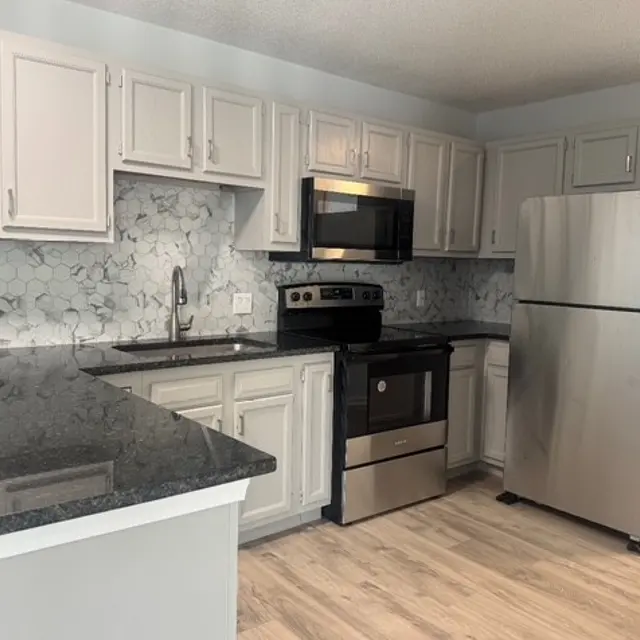 A modern kitchen featuring white cabinets, a gray granite countertop, stainless steel appliances, and a patterned backsplash.