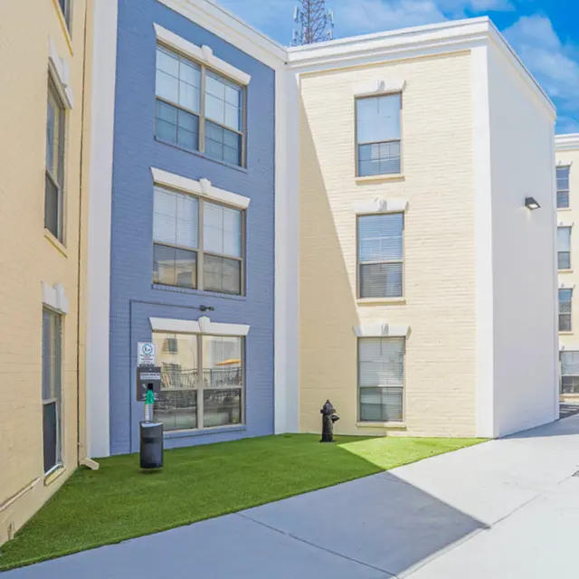 Exterior view of a multi-story apartment building featuring yellow and gray walls, large windows, and a small green lawn area.