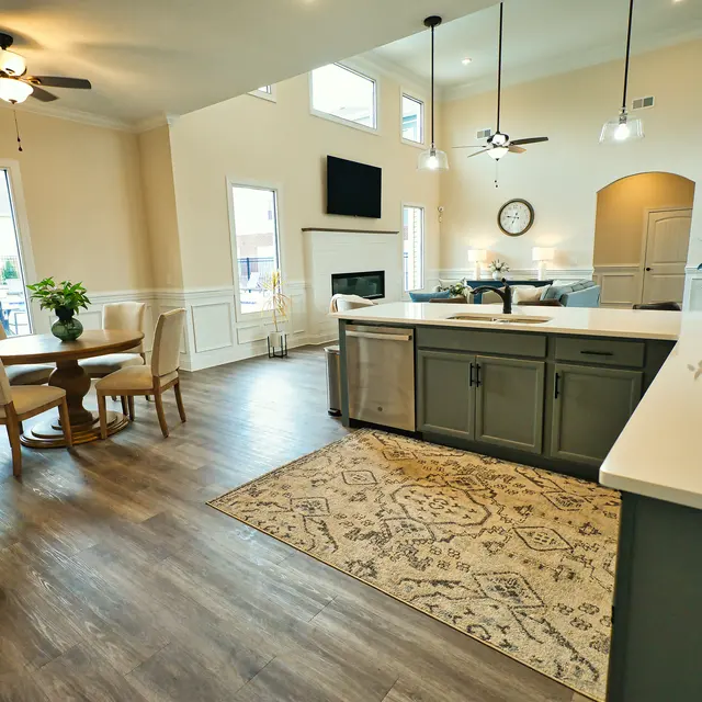 An open concept kitchen and living room with a dining table and chairs, a stylish kitchen island, and bright lighting, featuring a large window and a cozy fireplace.