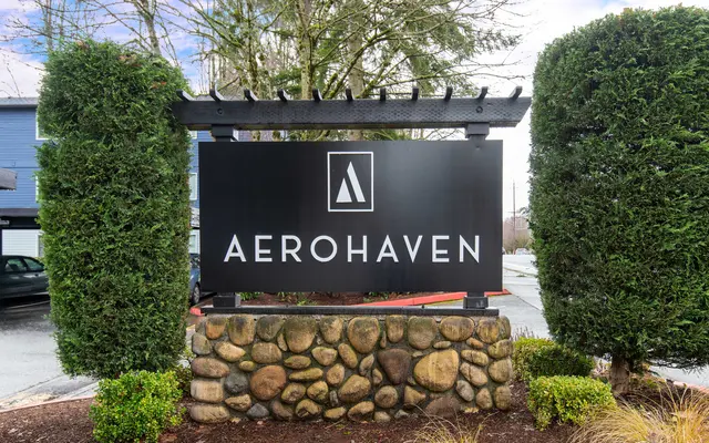 Sign for AeroHaven, featuring a modern logo and stone base, surrounded by greenery.