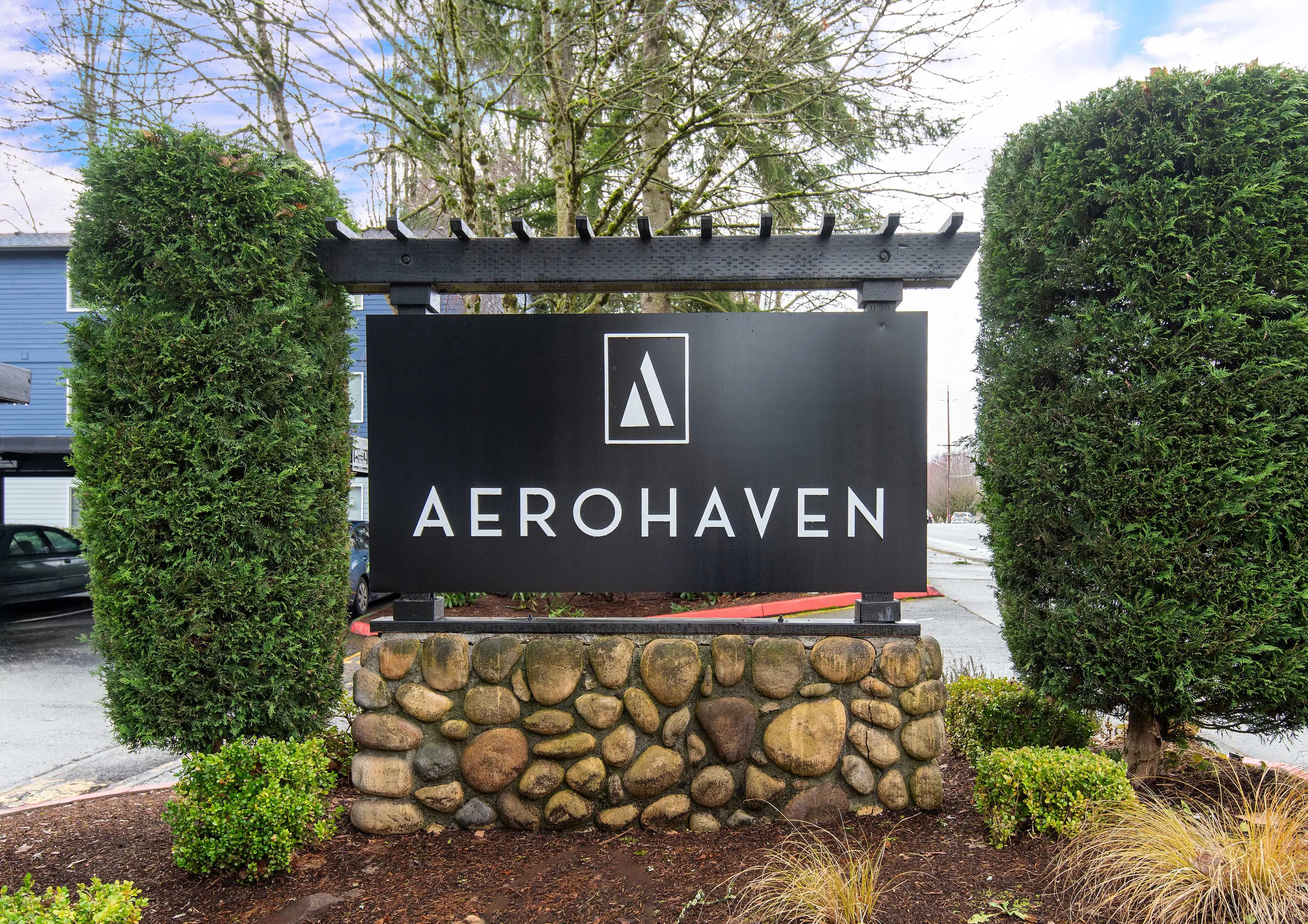 Sign for AeroHaven, featuring a modern logo and stone base, surrounded by greenery.