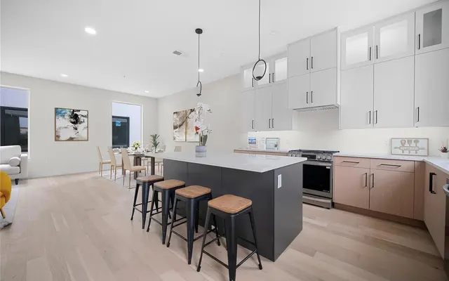 A modern kitchen and living area with an open layout, featuring a large island with stools, stylish cabinets, and dining space.