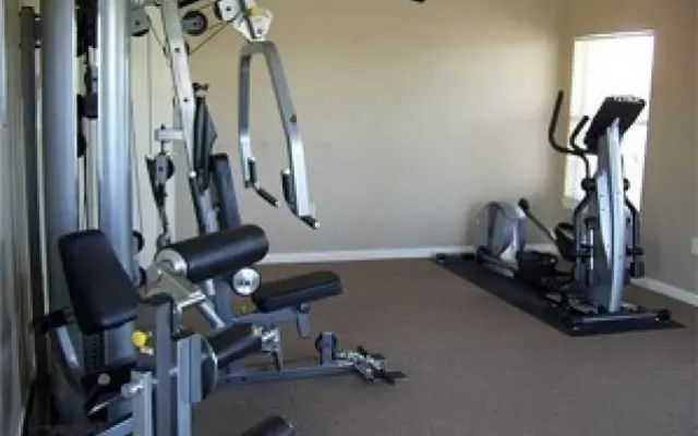 A home gym featuring a multi-station workout machine and an elliptical machine against a light-colored wall.