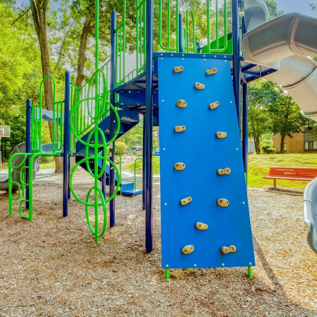 Colorful playground featuring a climbing wall and slide surrounded by trees.