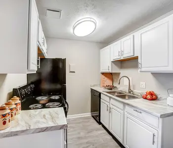 A modern kitchen featuring white cabinetry, stainless steel appliances, and a marble countertop. The kitchen includes a black stove, a sink with a faucet, and a few decorative items such as a kettle and fruit in a bowl.