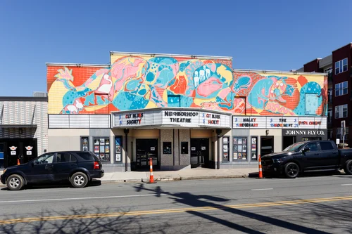 Colorful mural on the exterior of a theater building with cars parked in front.