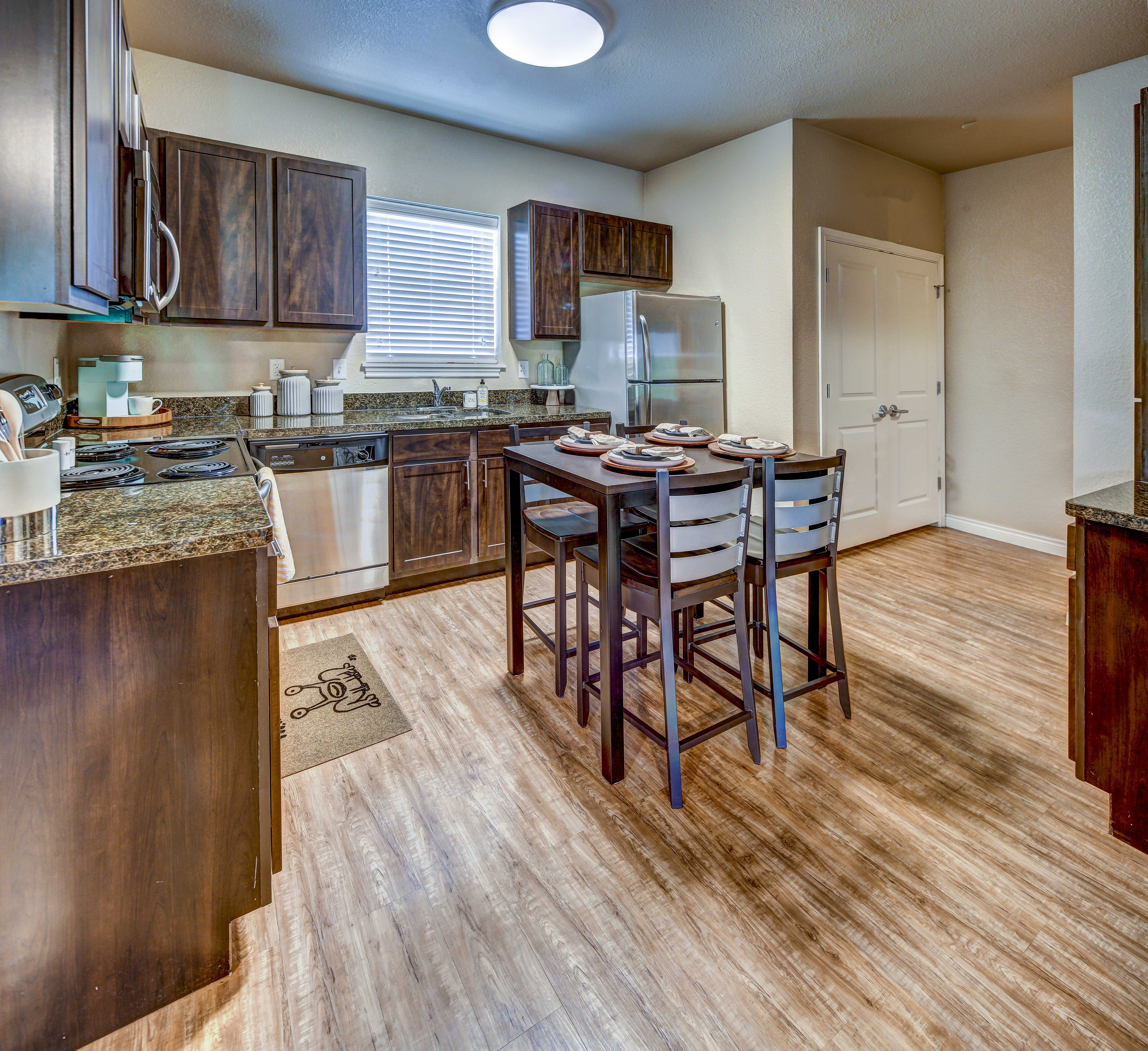 Modern Kitchen Interior A modern kitchen with dark wood cabinets, granite countertops, and stainless steel appliances. A dining table with four chairs is situated in the center, set for a meal, while a window lets in natural light.