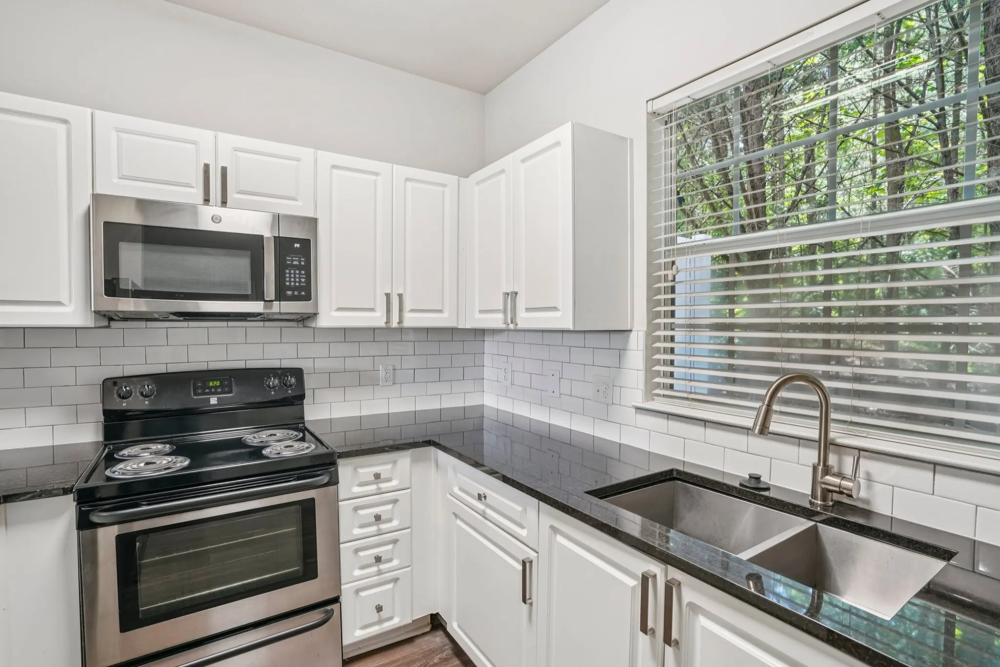 A modern kitchen featuring white cabinets, stainless steel appliances, and black countertops, with a window providing natural light.