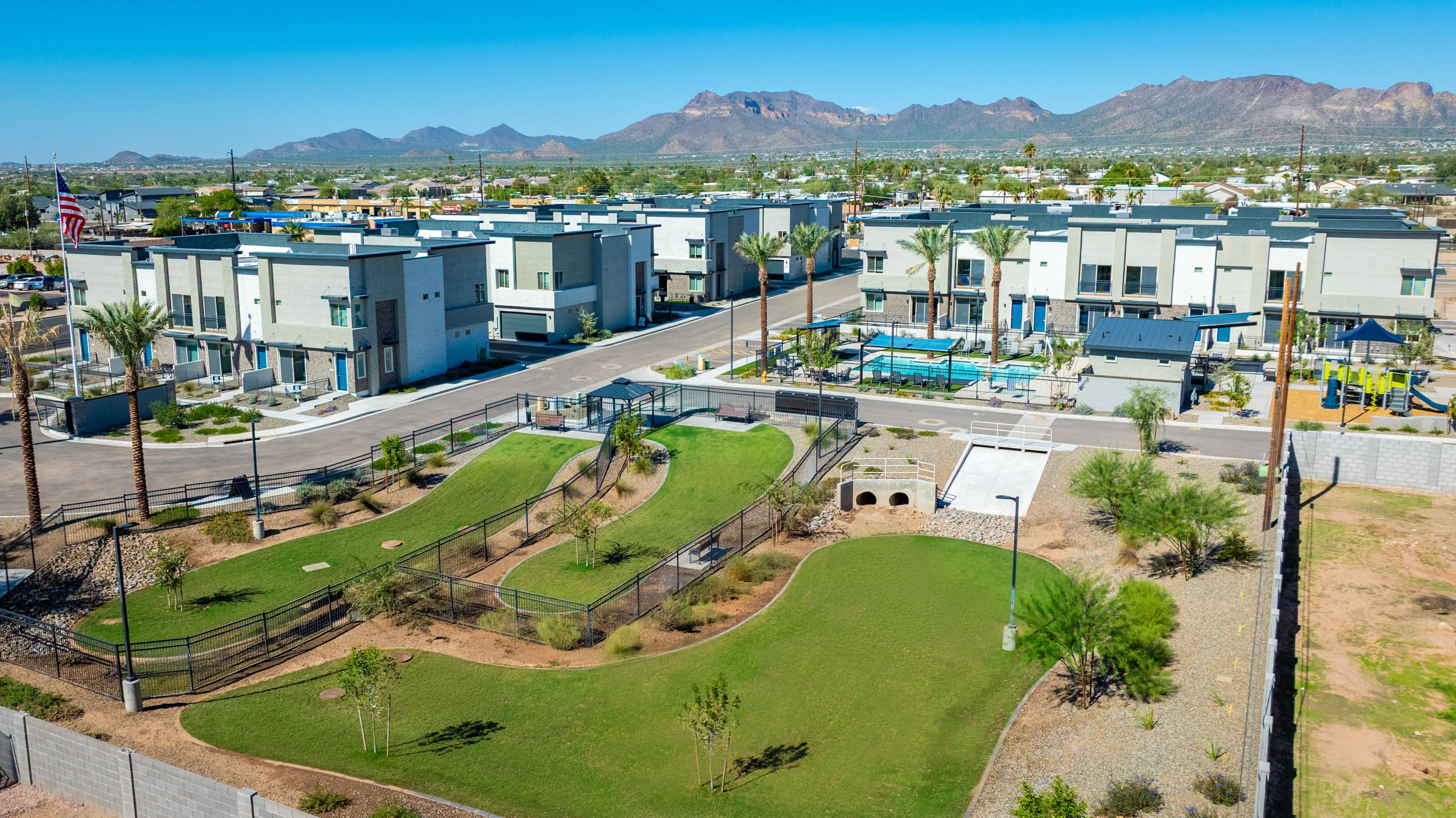 Aerial view of a modern residential complex featuring multiple buildings, a swimming pool, and landscaped green areas including playgrounds.