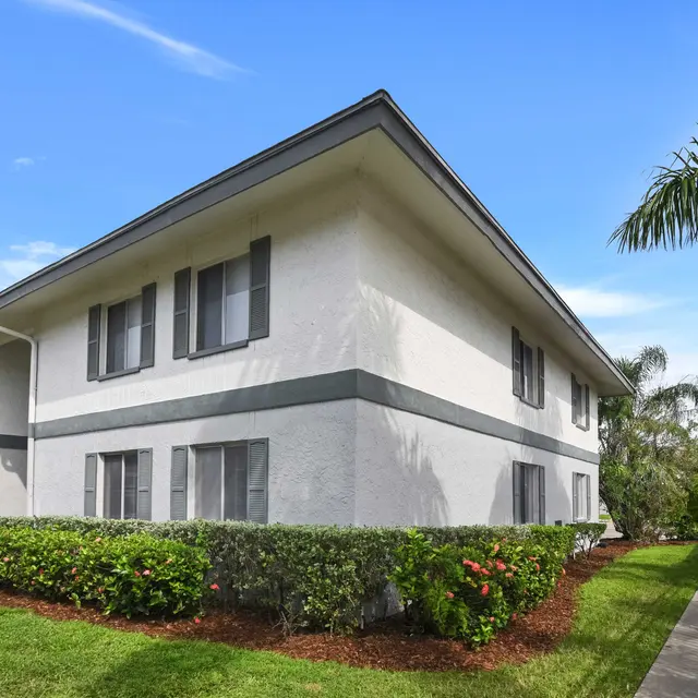 Side view of a two-story apartment building surrounded by greenery and palm trees.
