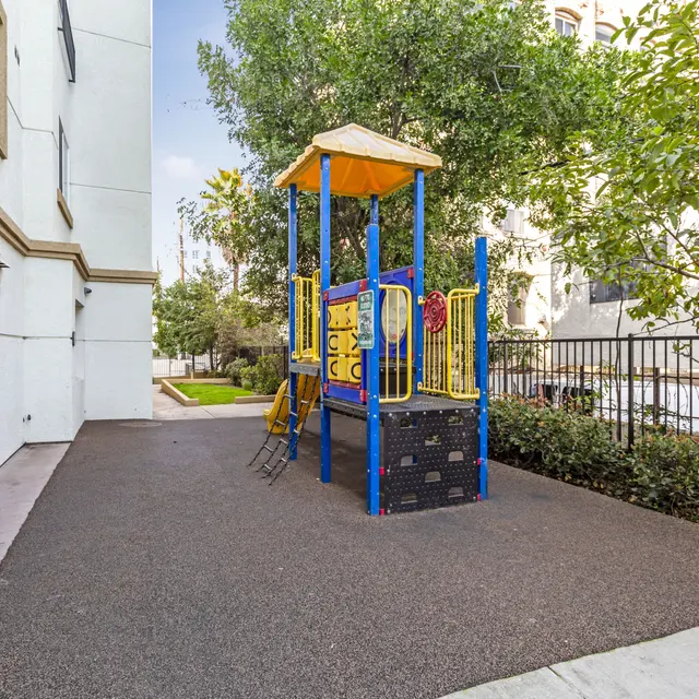 A small playground with colorful equipment surrounded by trees and a fence in a residential area.