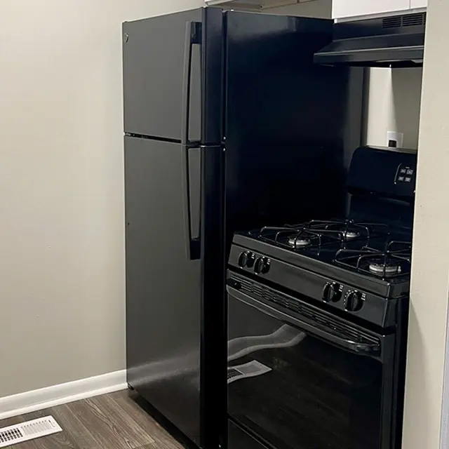 A compact kitchen area featuring a black refrigerator and a black gas stove situated against a light grey wall.