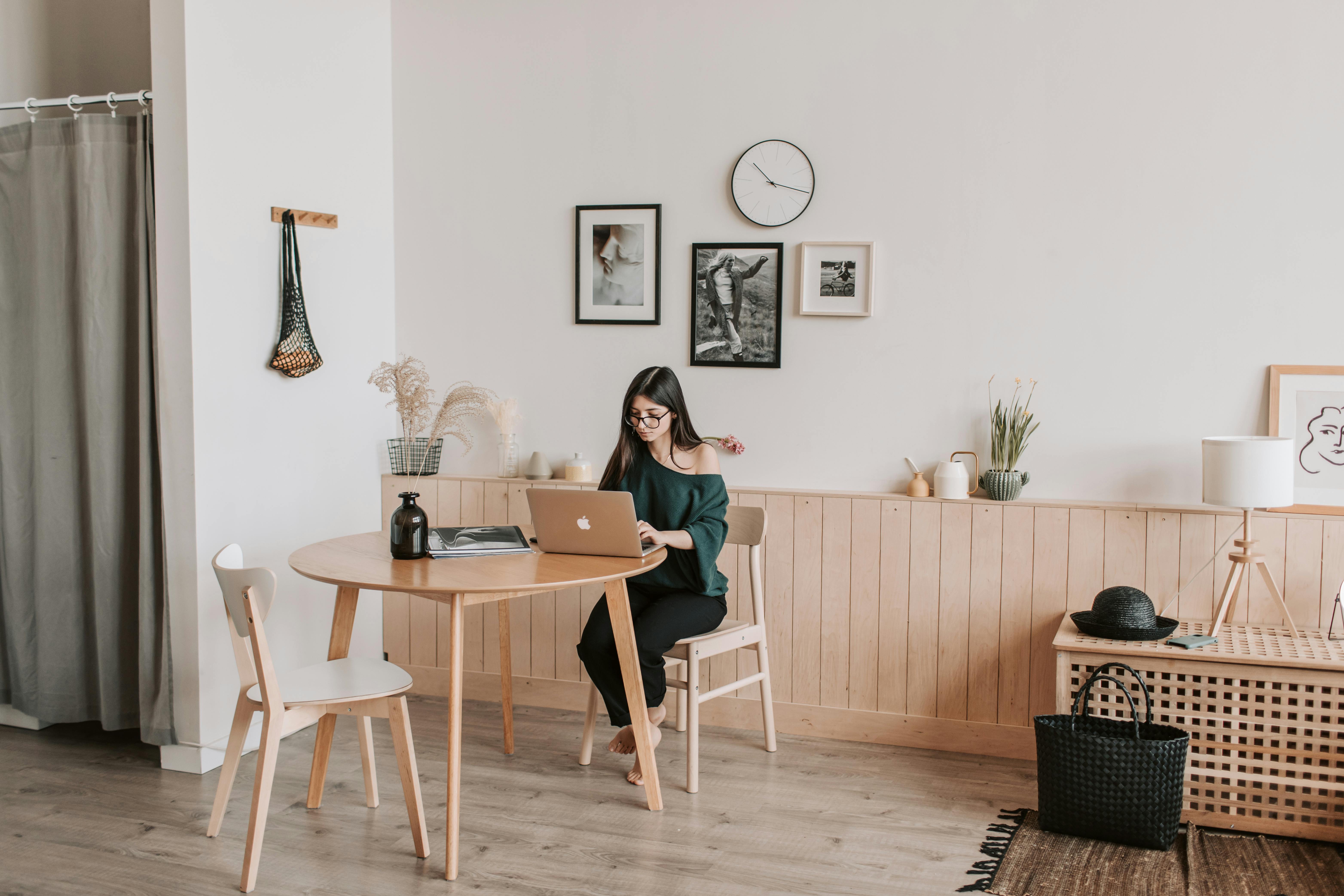 A woman sitting at a wooden table working on a laptop in a modern home office, with minimalistic decor.