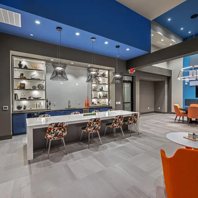 Interior view of a contemporary living space featuring a long white table, colorful chairs, and a blue-accented wall.