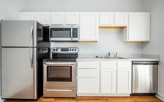A modern kitchen featuring stainless steel appliances, including a refrigerator, stove, microwave, and dishwasher, with white cabinets and a wooden floor.