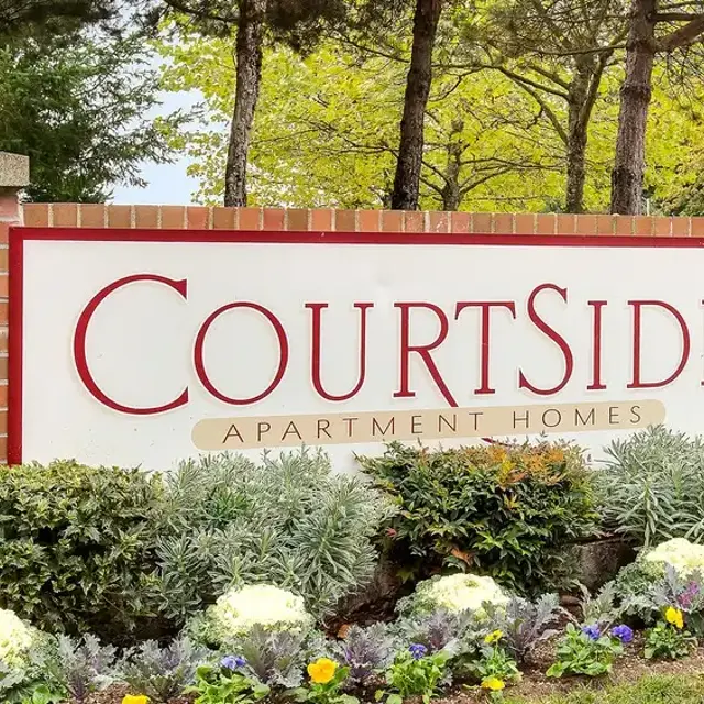 Sign for Courtside Apartment Homes surrounded by greenery and flower beds.
