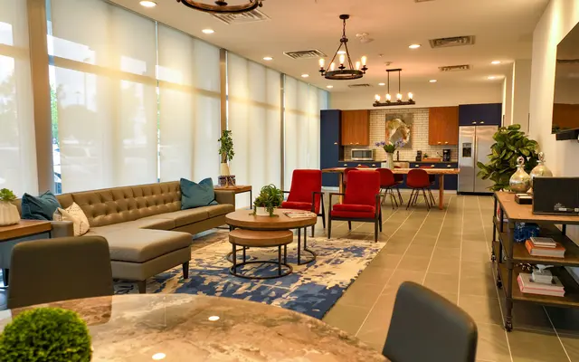 A modern living space with a cozy seating arrangement featuring a grey couch and red chairs. The room is well-lit with large windows and a decorative rug on the floor.