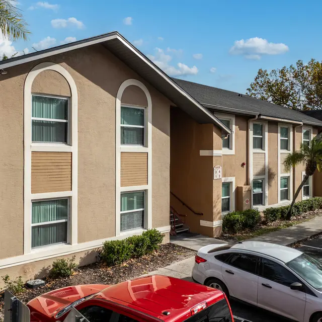 A two-story apartment building with several windows, surrounded by trees and parking spaces.