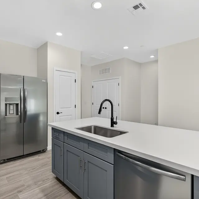 A modern kitchen featuring a central island with a sink, gray cabinetry, stainless steel appliances, and light-colored walls.