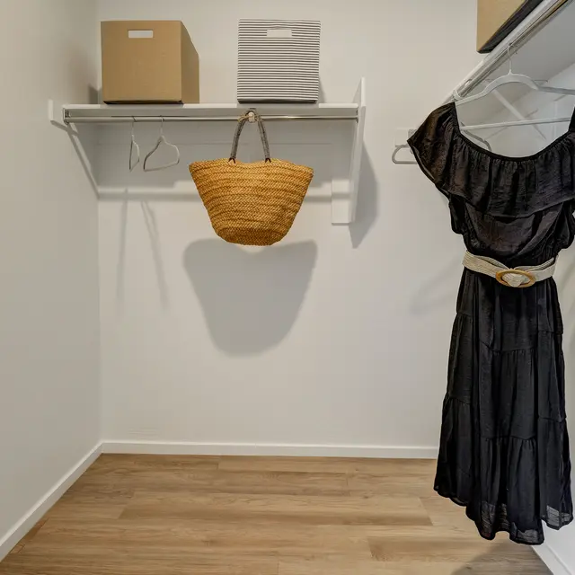 A minimal closet featuring a black dress on a hanger, a woven bag, and two storage boxes on a shelf.