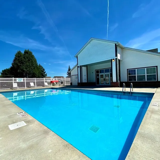 A clear blue swimming pool with a white fence surrounding it and a building with large windows in the background under a clear blue sky.