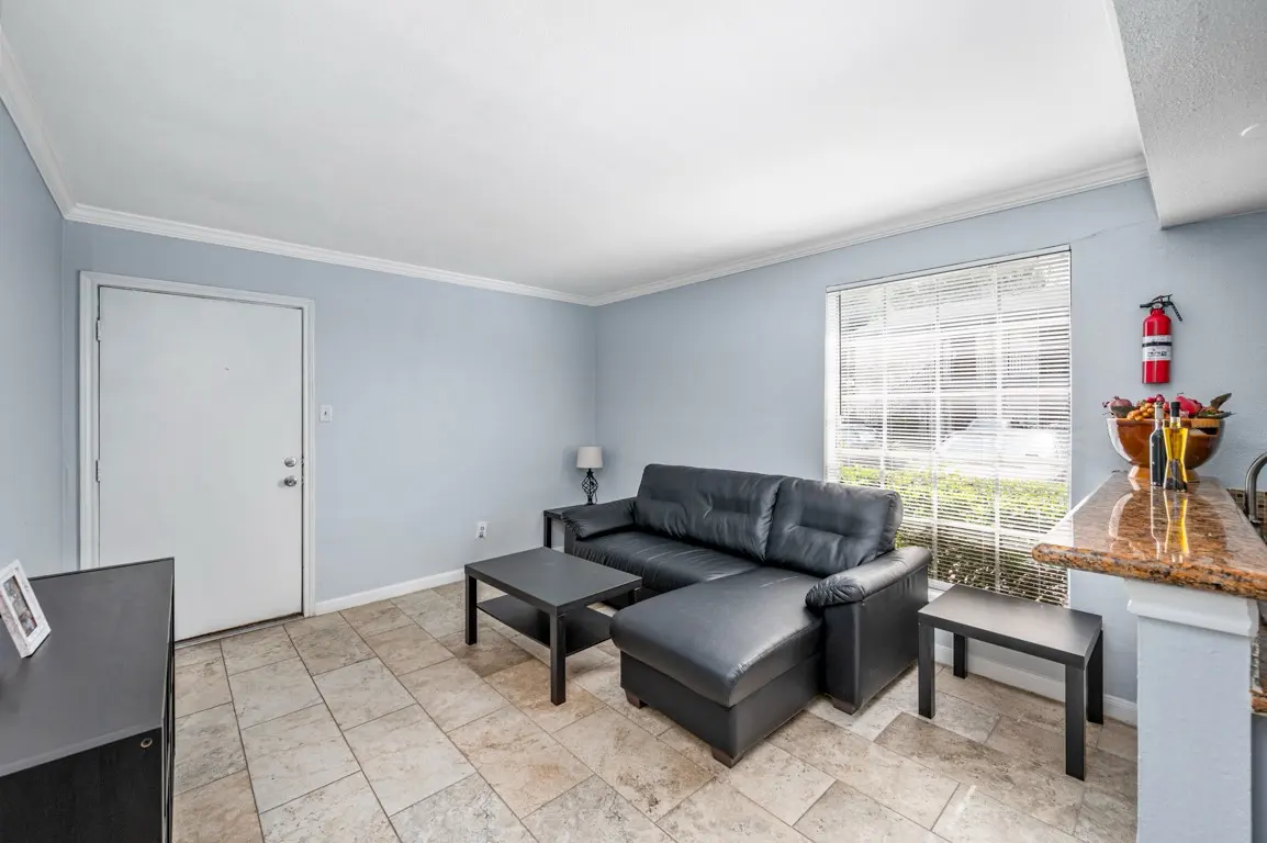 A cozy living room featuring a black leather sectional sofa, a dark wood coffee table, and a light blue wall with a window.