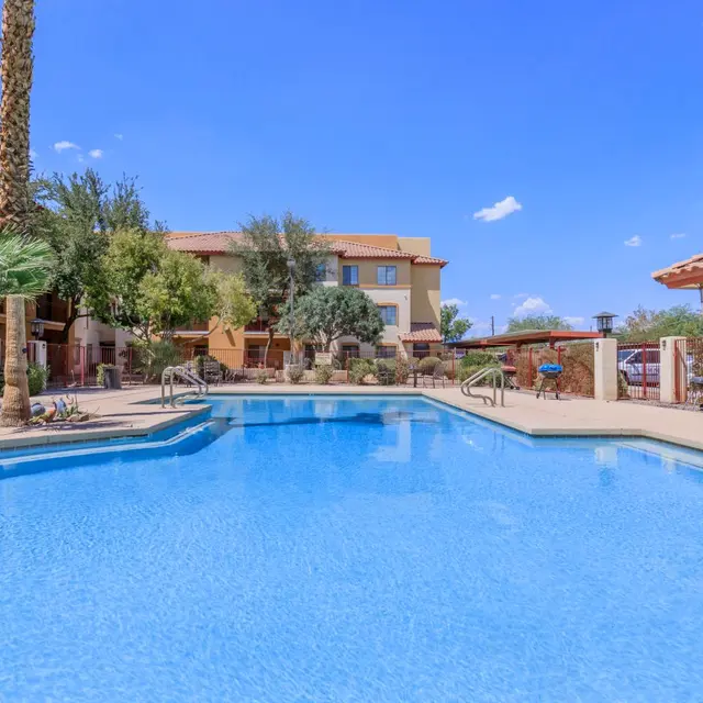Resort Pool Area A clear blue swimming pool surrounded by palm trees and a resort building in a sunny environment.