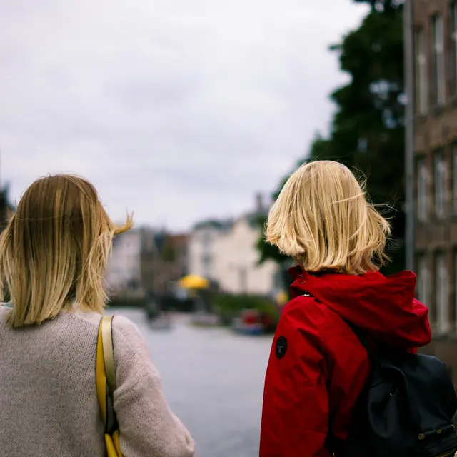 Two young women standing with their backs to the camera, looking at a canal lined with buildings.