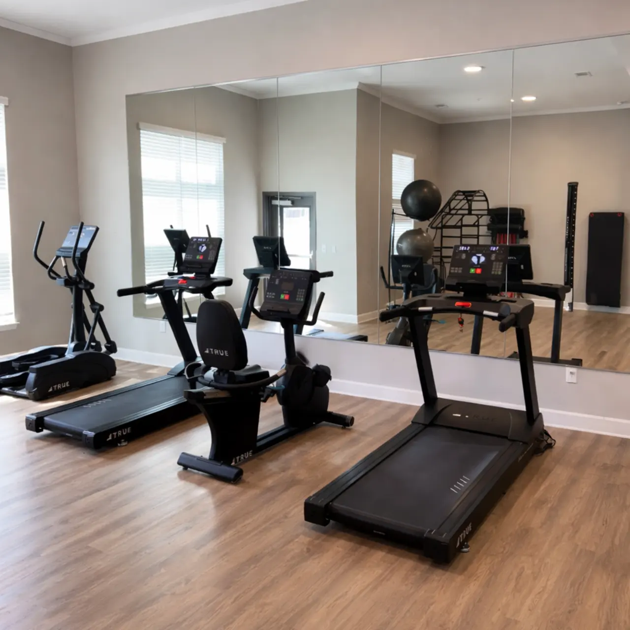 A modern gym interior featuring exercise equipment including an elliptical machine, stationary bike, and treadmill, with a large mirror reflecting the workout area.