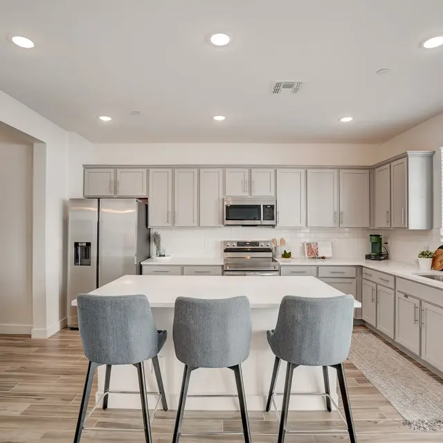Stylish Modern Kitchen A modern kitchen with gray cabinetry, stainless steel appliances, and an island with three stools. The room is brightly lit with recessed lighting and has a neutral color palette.