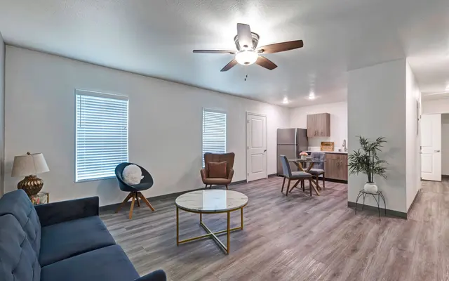 Modern Living Room Design A spacious and modern living area featuring a blue sofa, a round coffee table, and various seating options. There are two windows with white blinds allowing natural light into the space.