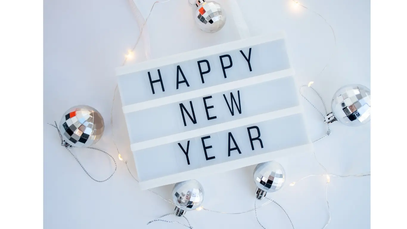 A lightbox sign displaying the message 'HAPPY NEW YEAR' surrounded by silver disco balls and fairy lights on a white surface.
