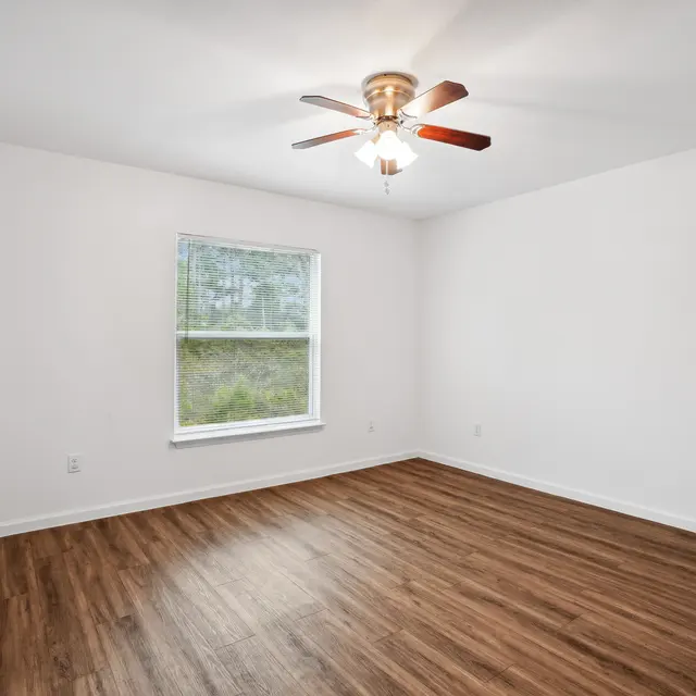 Empty Room with Natural Light An empty room with a wooden floor, a ceiling fan, and a window letting in natural light.