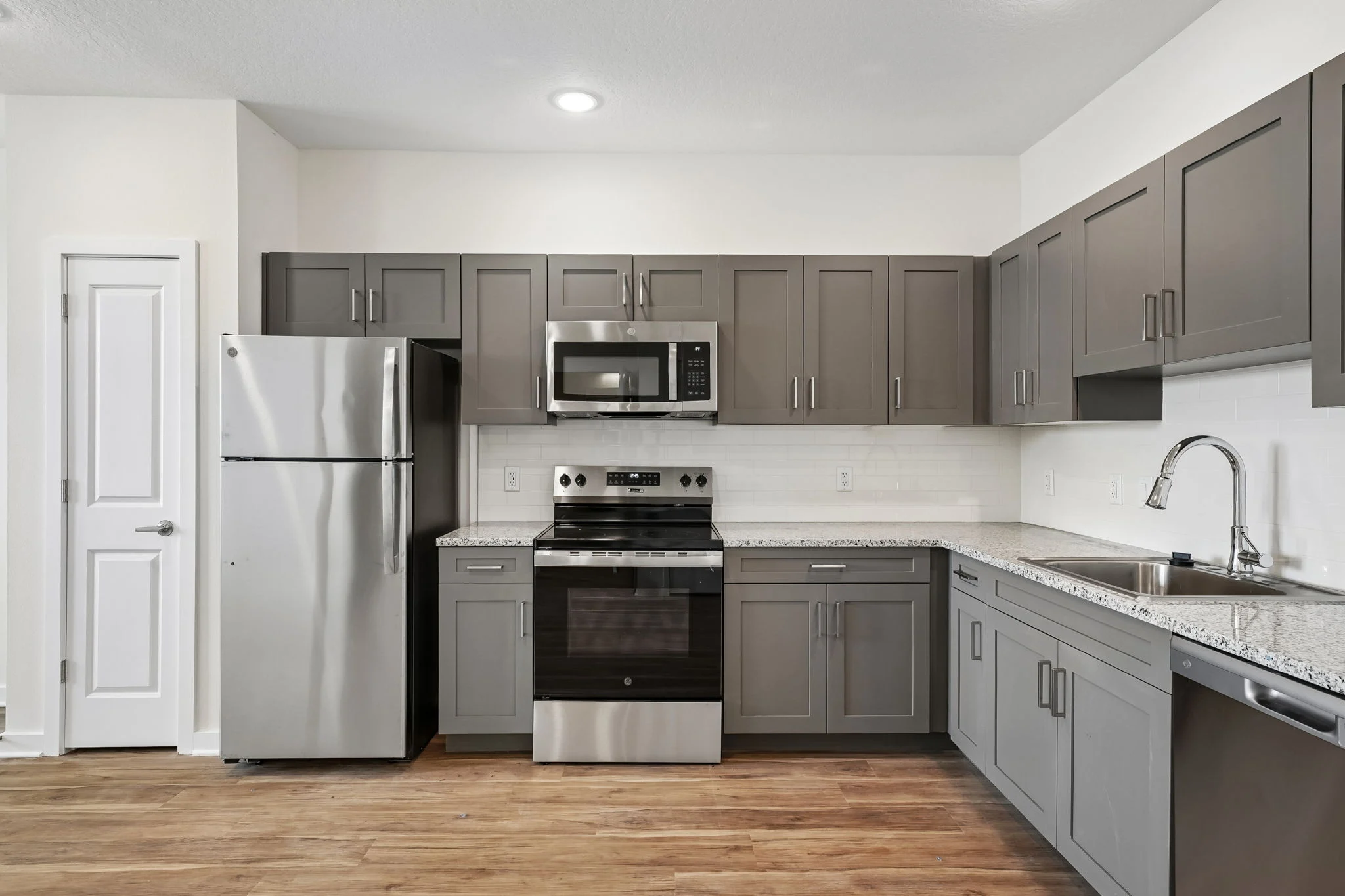 A modern kitchen featuring dark gray cabinets, stainless steel appliances including a refrigerator, microwave, and stove, and a granite countertop.