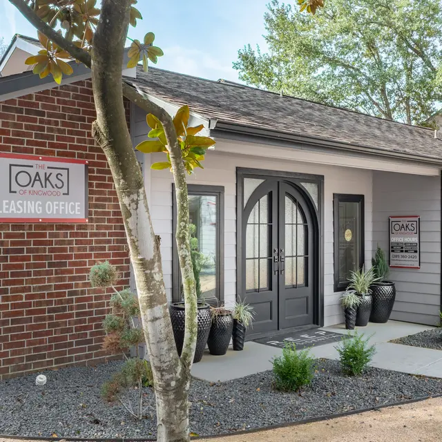 Exterior view of a leasing office building with a brick and white facade, featuring a sign that reads 'OAKS LEASING OFFICE'.