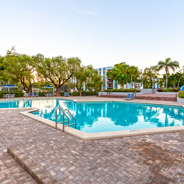 Swimming Pool Area A scenic swimming pool area with two pools surrounded by greenery and palm trees, featuring lounge chairs and a well-paved patio.