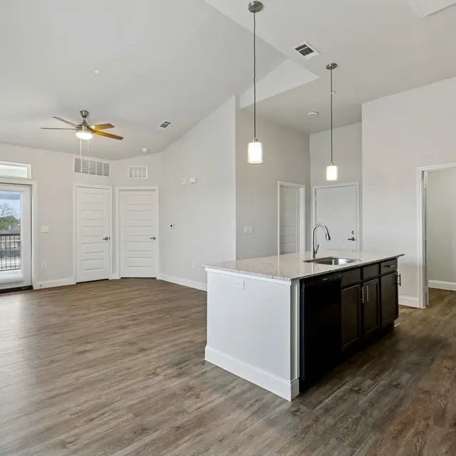 Modern apartment interior featuring an open floor plan, light wood flooring, a kitchen island, and large windows with a view.
