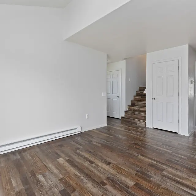Empty Room Interior Interior view of a room with wooden flooring, white walls, and a staircase in the background.