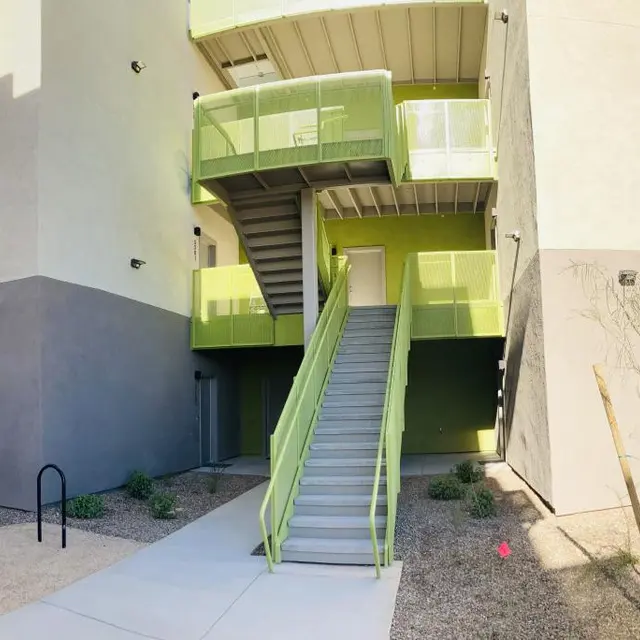 Modern Apartment Building Exterior A modern apartment building showing a staircase leading to the upper floors with green accents and a clear blue sky in the background.