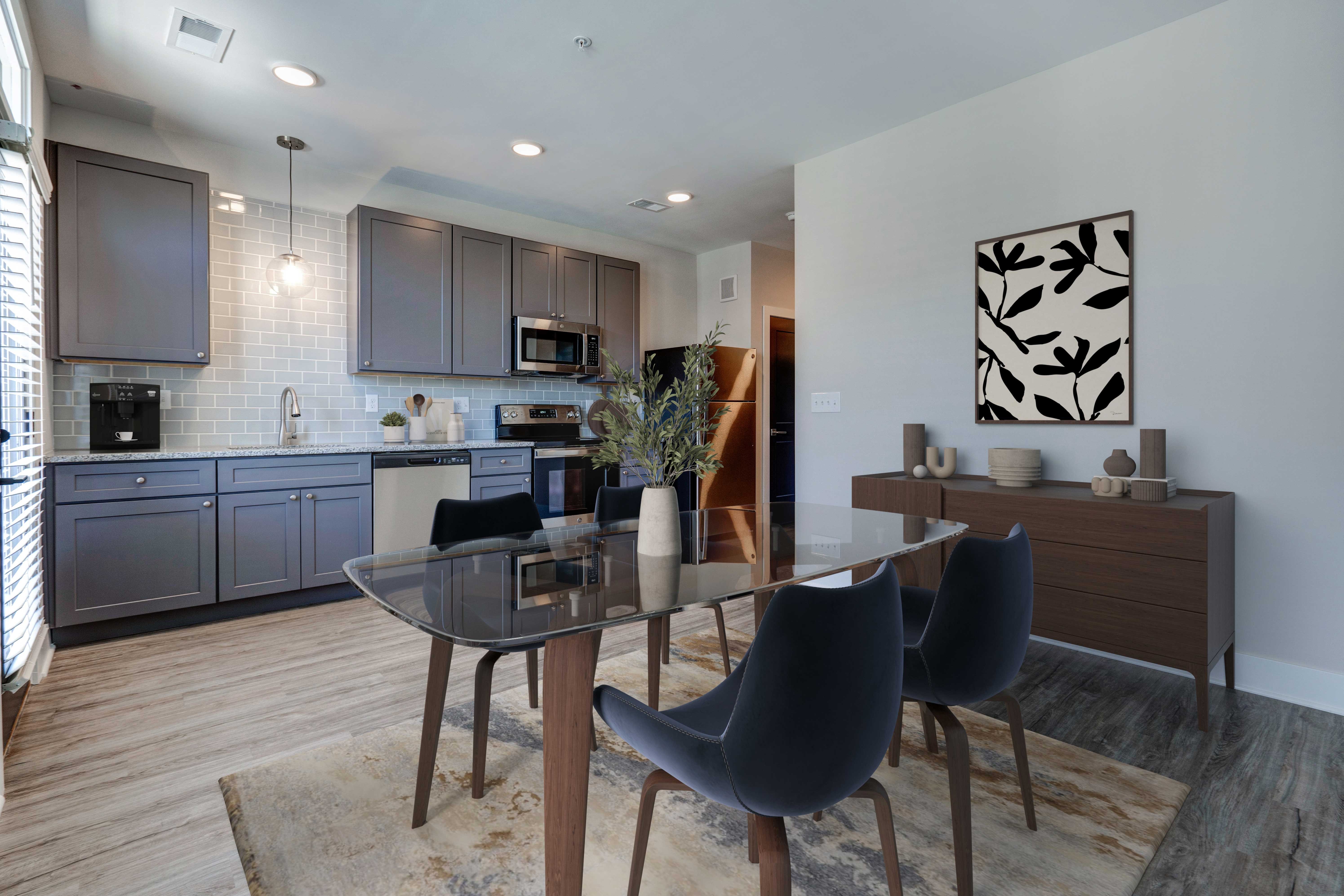 Modern Kitchen and Dining Space A modern kitchen and dining area featuring a glass dining table surrounded by black chairs, with an organized kitchen on the left showcasing grey cabinets and stainless steel appliances.