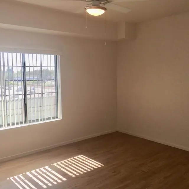 An empty room with a large window allowing natural light to enter, showcasing wood-like flooring and a ceiling fan.