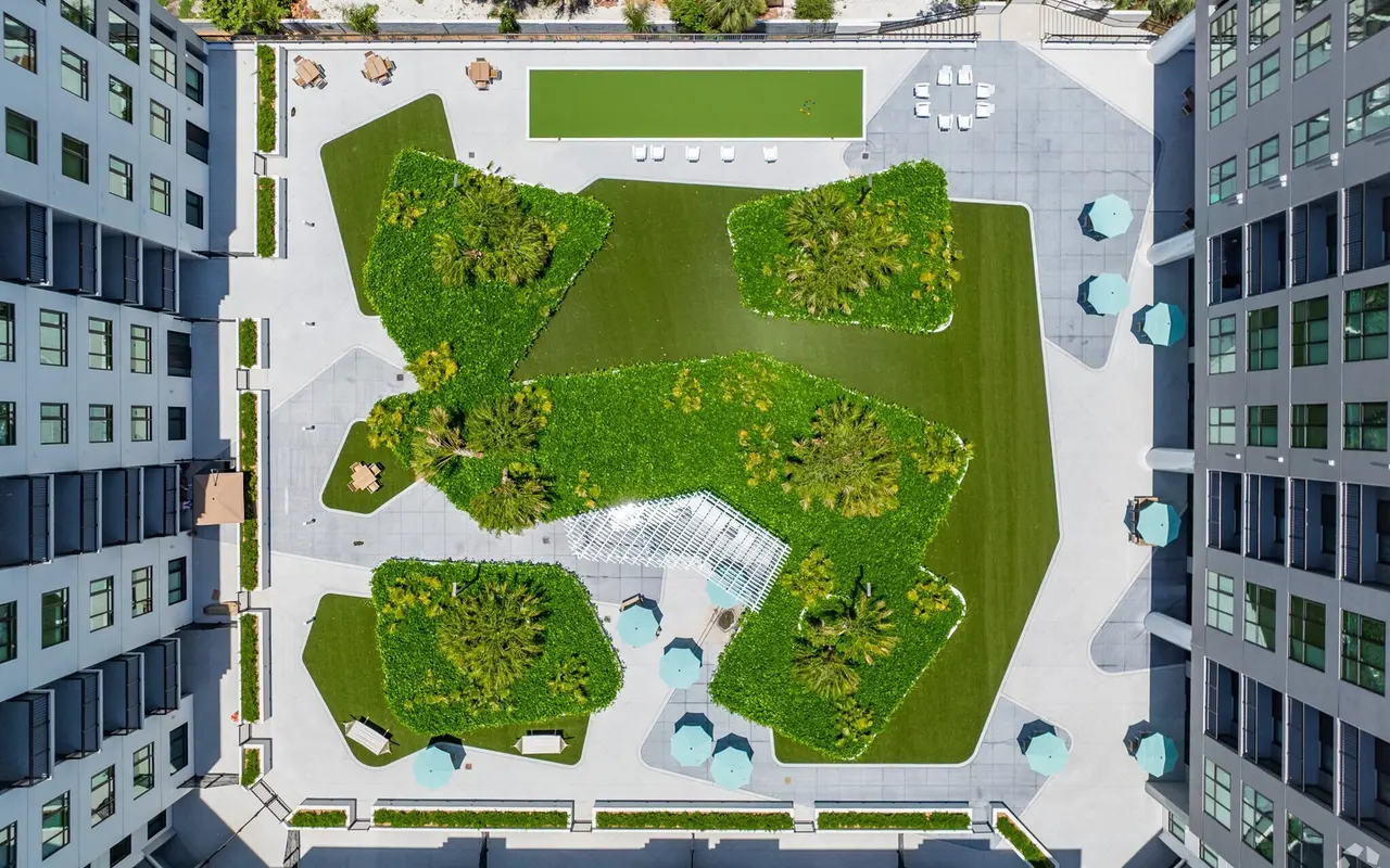 Aerial view of a modern urban green space featuring various landscaped areas, seating arrangements, and a lawn in a city setting.