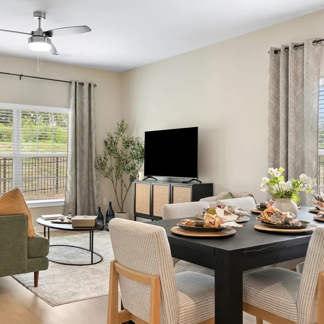 A stylish living room with a green sofa, decorated dining table, and television.