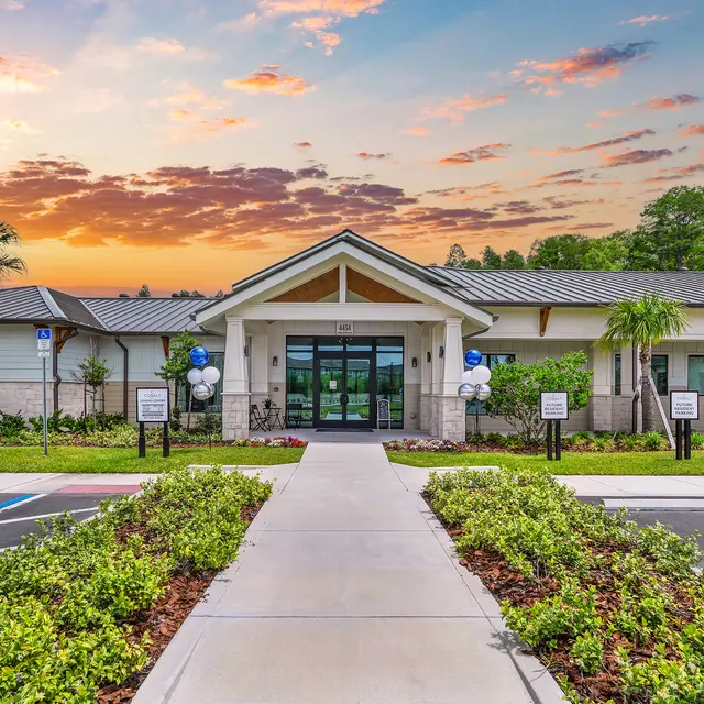Community Center at Sunset A newly constructed community center with a modern architectural design, surrounded by greenery and palm trees, under a colorful sunset sky.