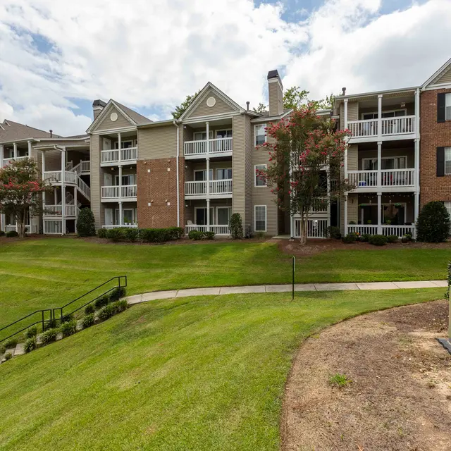 Exterior view of a multi-unit apartment complex with green lawns and a pathway.