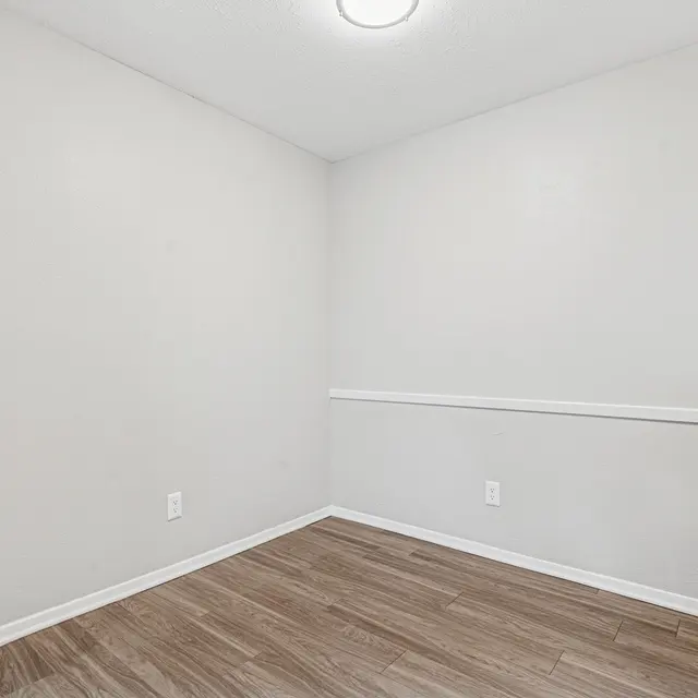 An empty room with light gray walls and wooden flooring.
